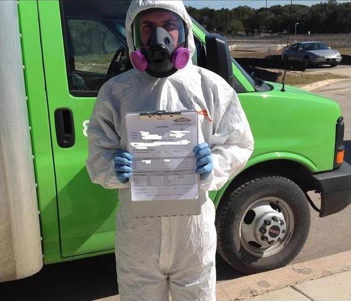 man in bio hazard suit holding mold certification certificate